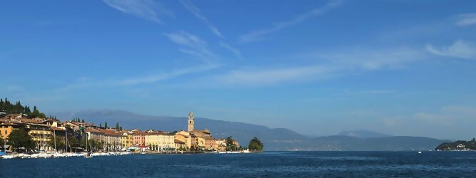 Trip EU beliebte Urlaubsziele am Gardasee -  Mit einer Fläche von 370 km² ist der Gardasee der größte See Italiens. Es liegt am Fuße der Alpen und erstreckt sich über drei Staaten: Lombardei, Venetien und Trentino. Die maximale Tiefe des Sees beträgt 346 m, er hat eine längliche Form und sein nördliches Ende ist sehr schmal. Dort ist der See von den Bergen der Gruppo di Baldo umgeben. Du trittst aus deinem gemütlichen Hotelzimmer und es begrüßt dich die warme italienische Sonne. Du blickst auf den atemberaubenden Gardasee, der in zahlreichen Blautönen schimmert - von tiefem Dunkelblau bis zu funkelndem Türkis. Majestätische Berge umgeben dich, während die Brise sanft deine Haut streichelt und der Duft von blühenden Zitronenbäumen deine Nase kitzelt. Du schlenderst die malerischen, engen Gassen entlang, vorbei an farbenfrohen, blumengeschmückten Häusern. Vereinzelt unterbricht das fröhliche Lachen der Einheimischen die friedvolle Stille. Du fühlst dich wie in einem Traum, der nicht enden will. Jeder Schritt führt dich zu neuen Entdeckungen und Abenteuern. Du probierst die köstliche italienische Küche mit ihren frischen Zutaten und verführerischen Aromen. Die Sonne geht langsam unter und taucht den Himmel in ein leuchtendes Orange-rot - ein spektakulärer Anblick.